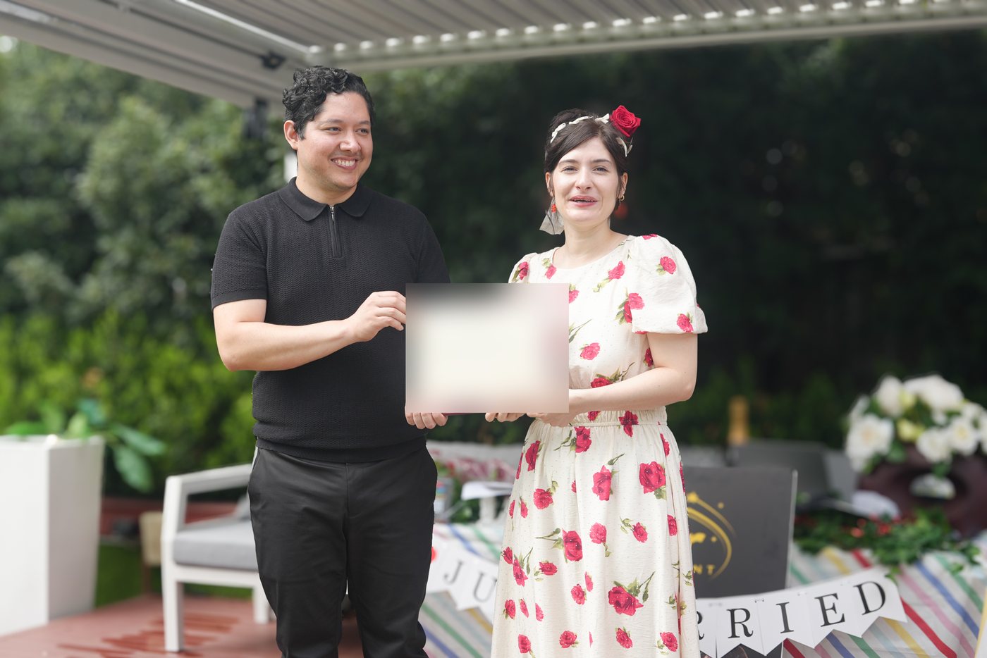 A couple holding their marriage certificate after a bilingual ceremony in Sydney, just-married bunting behind them