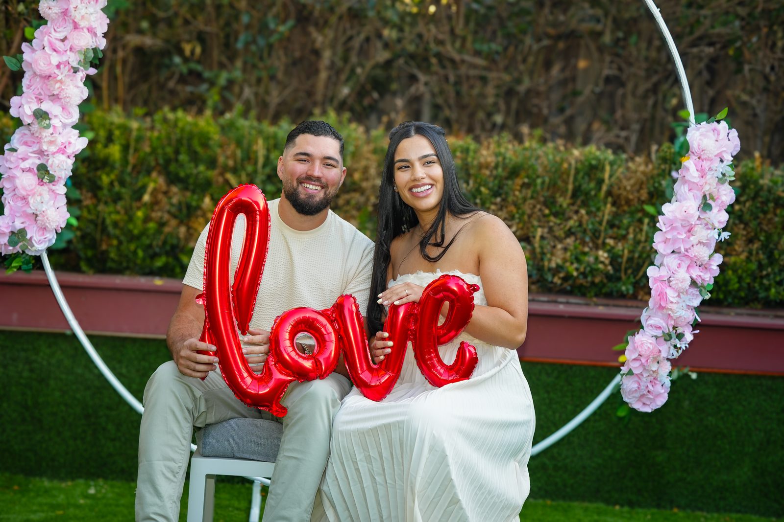 Pericles and Estafani smiling together with a red love balloon at their Brazilian garden wedding in Sydney