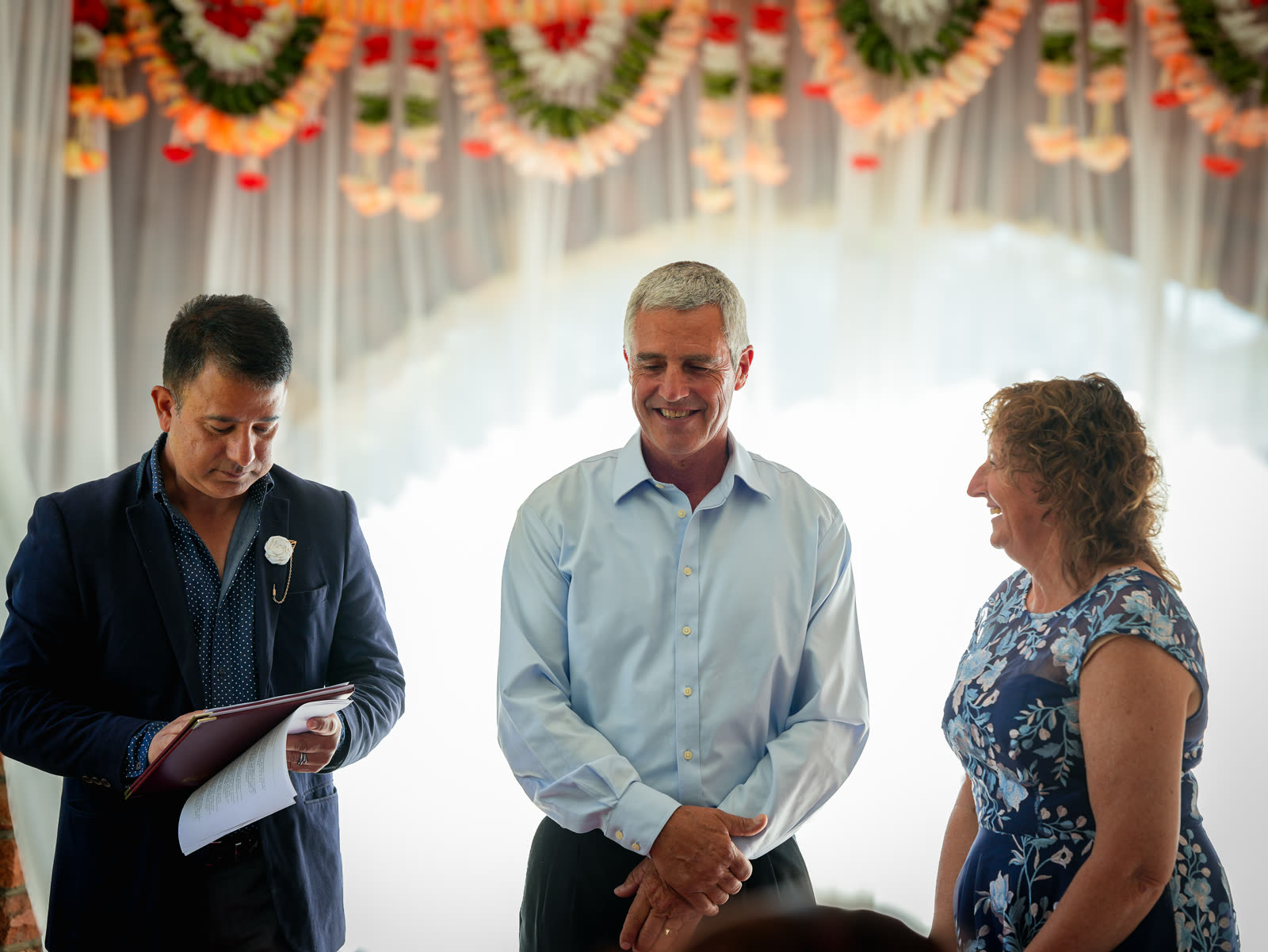 Star Celebrant reading from the ceremony folder while a smiling couple stand together beneath a flower garland arch in Sydney