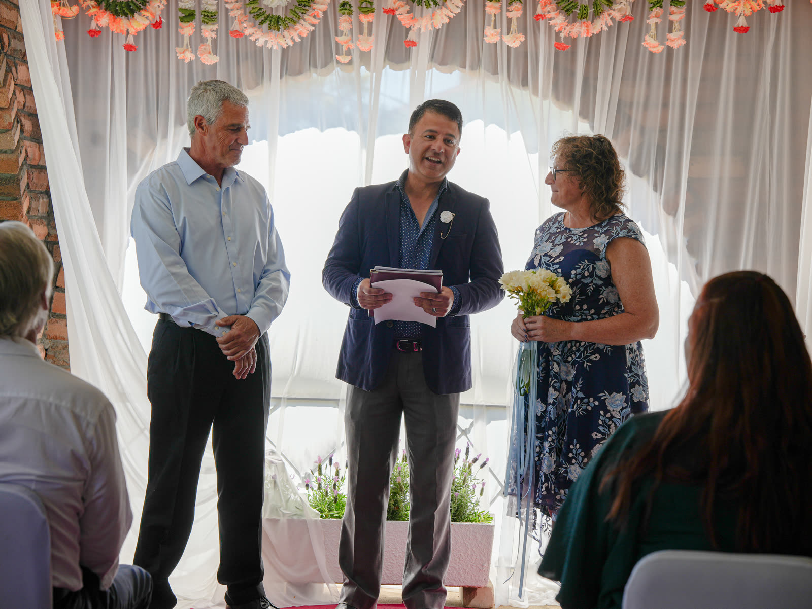 Star Celebrant officiating a wedding ceremony with the couple beneath a marigold and flower garland arch in Sydney