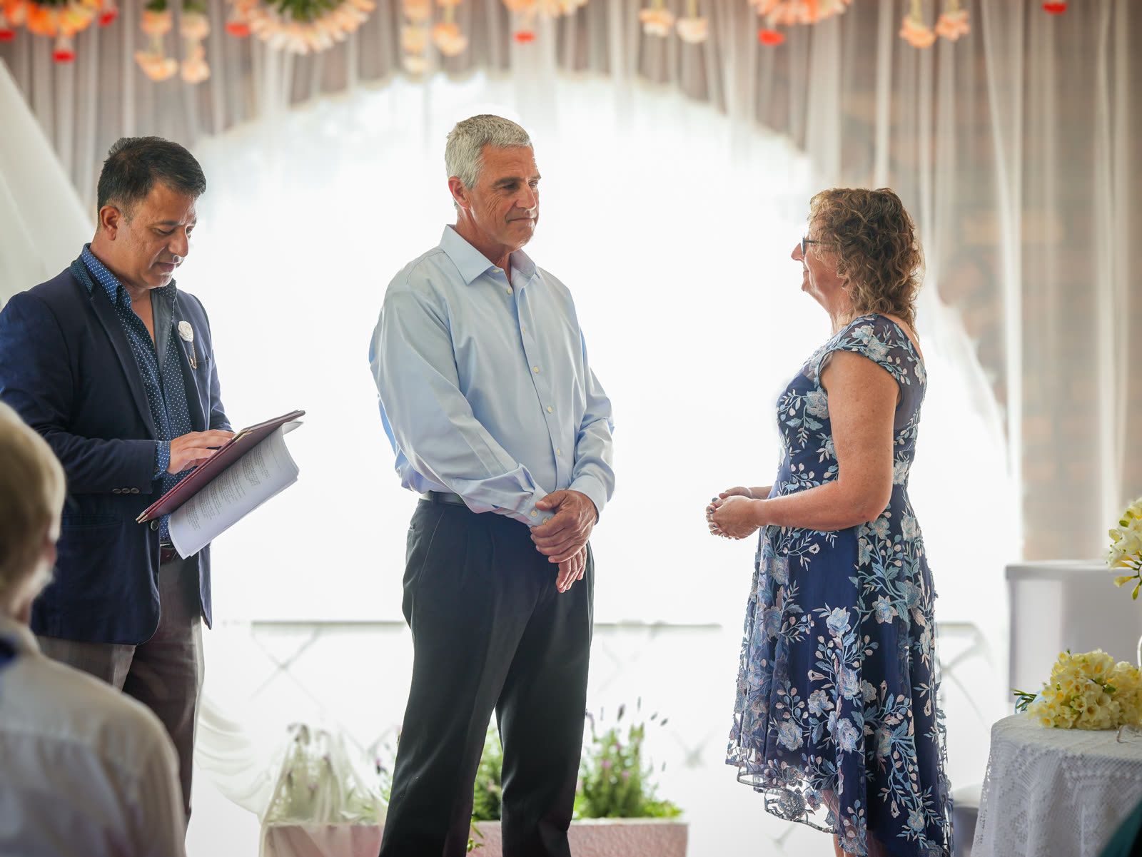 Marriage celebrant officiating a personalised wedding ceremony for a couple in front of a floral garland arch in Sydney