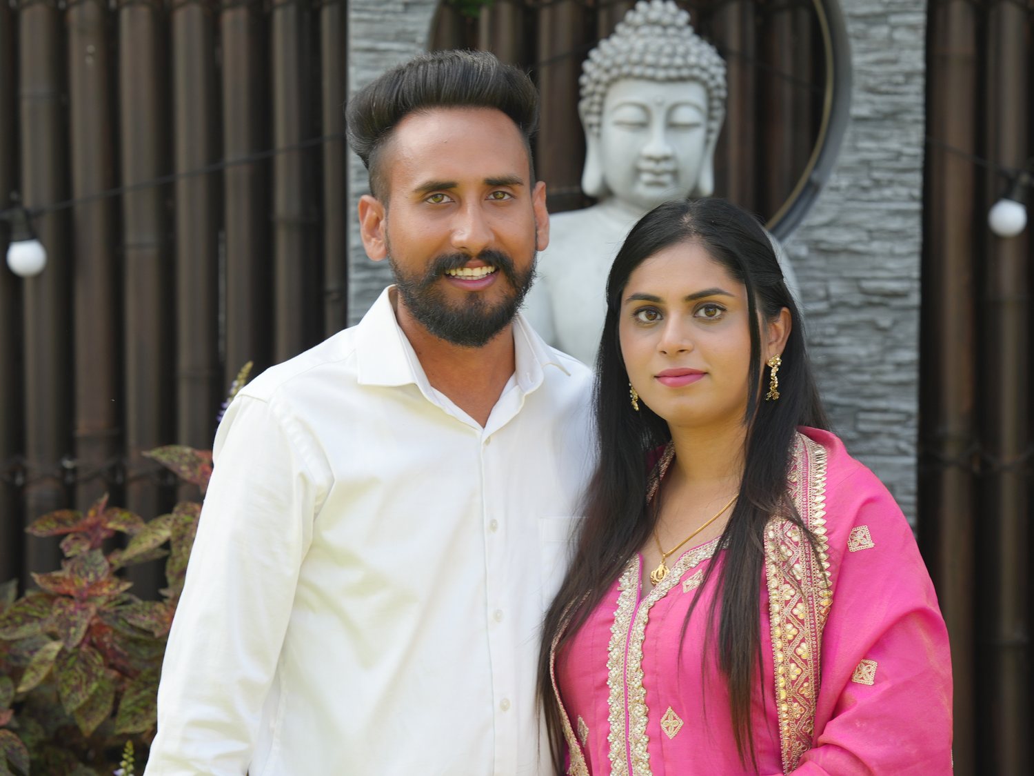 A couple standing together in a Sydney garden after their ceremony, Buddha statue behind them