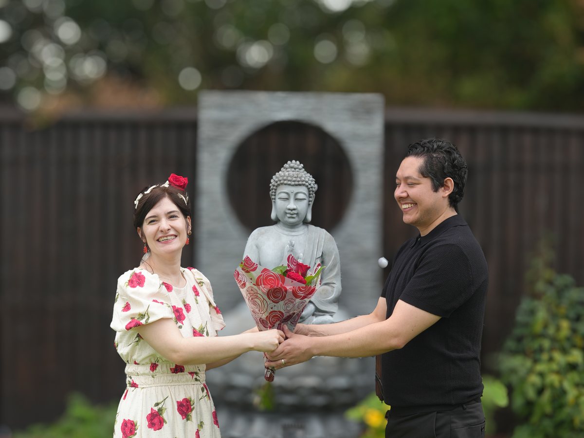 A couple laughing together holding a bouquet of red roses at their garden wedding in Sydney