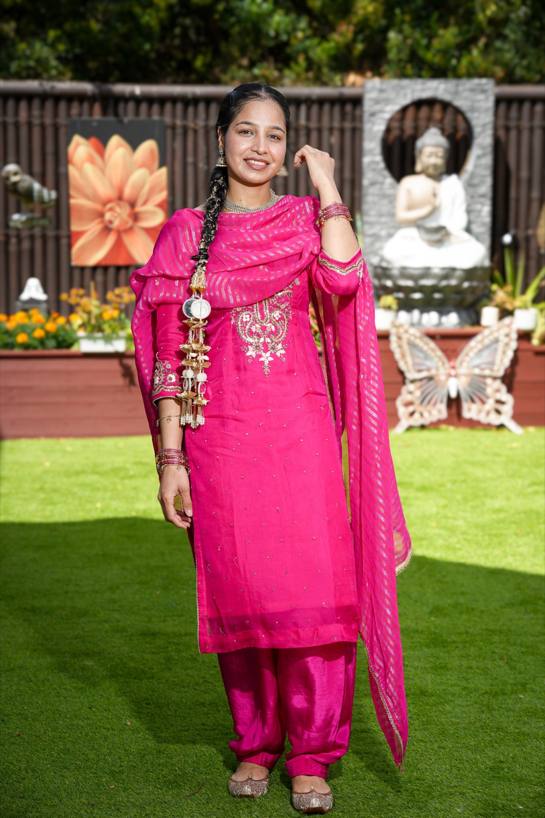 Harpreet in a pink embroidered Punjabi suit with a paranda tassel in her braid, standing on the lawn at her backyard wedding in Sydney