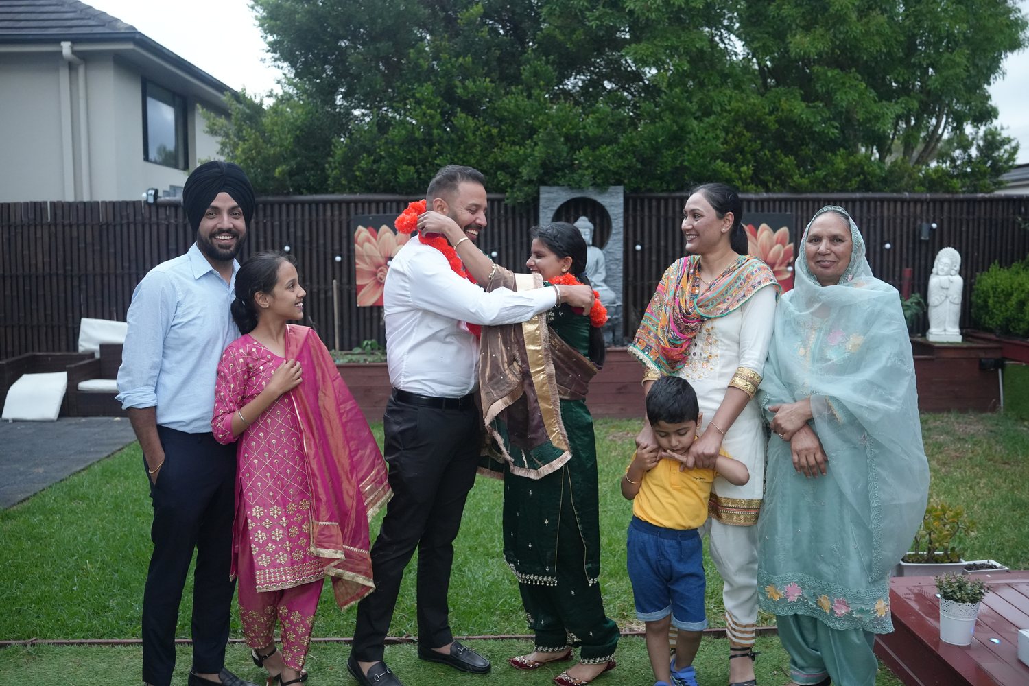 A couple exchanging marigold garlands surrounded by family at a Sydney garden ceremony