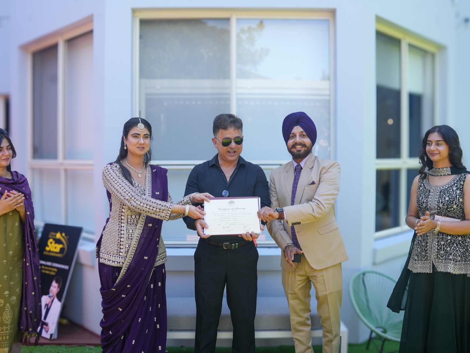 Celebrant Rohit Revo presenting Kanwarpal and Jashandeep with their marriage certificate while relatives look on at their garden wedding in Sydney