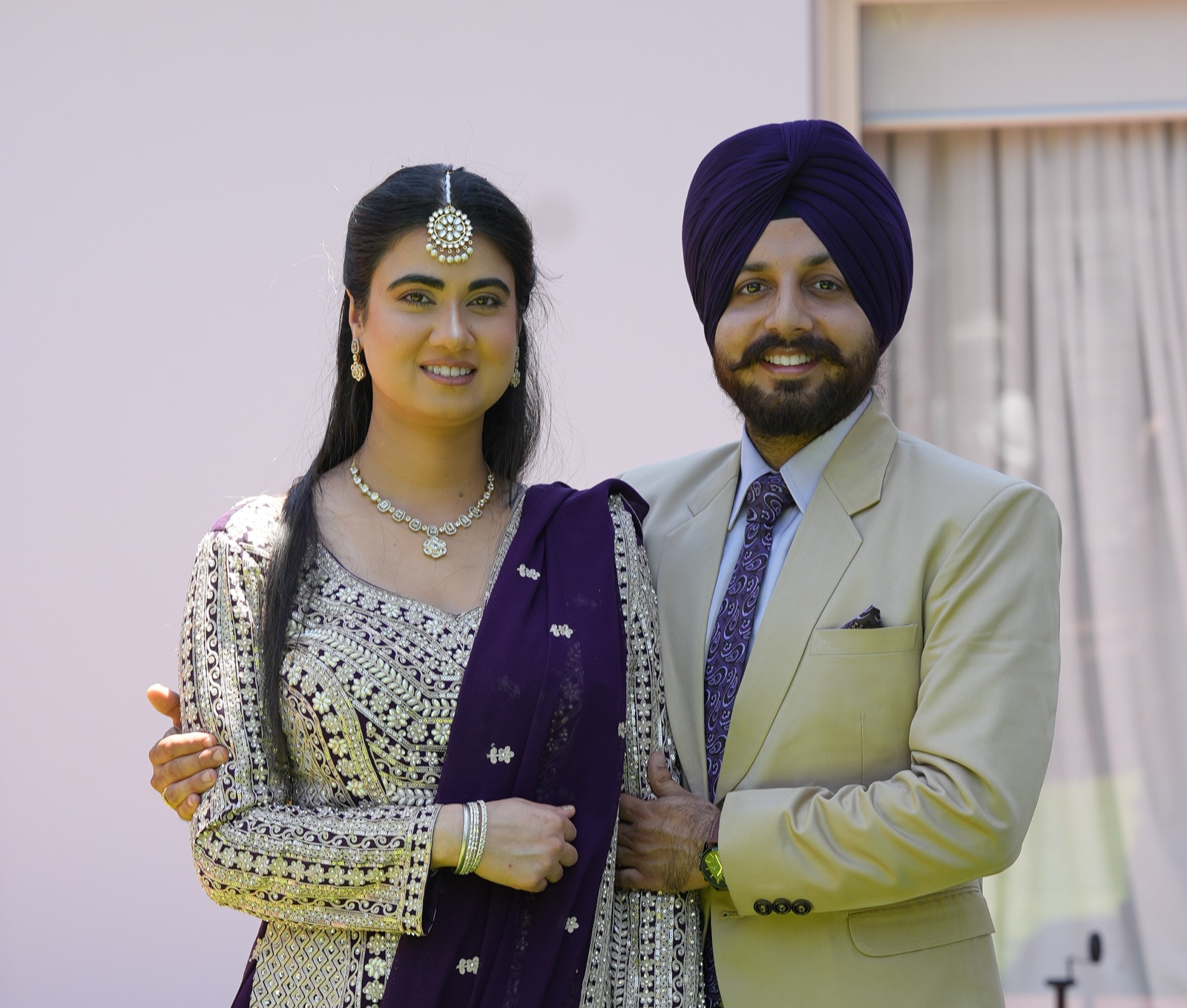 Kanwarpal and Jashandeep smiling together in a garden at their Sikh wedding in Sydney, she in plum purple and gold, he in a cream suit and purple turban