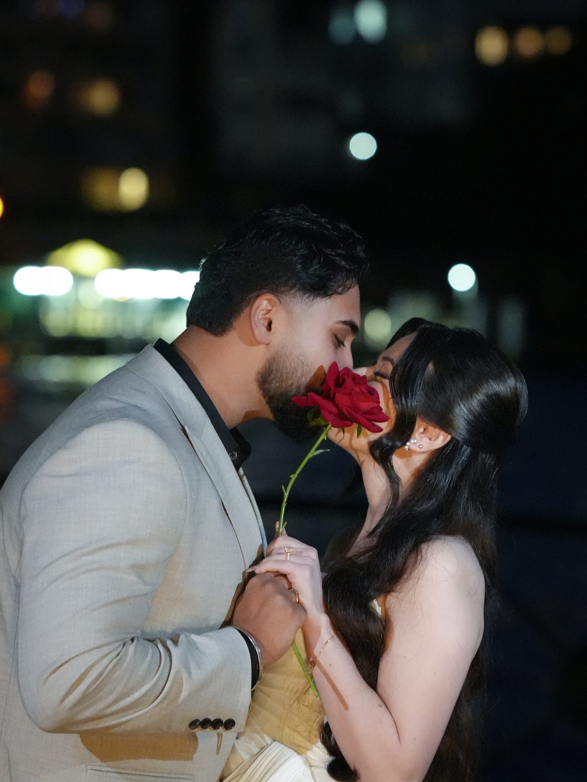 Couple sharing a kiss behind a red rose at their night-time engagement at Milsons Point, Sydney