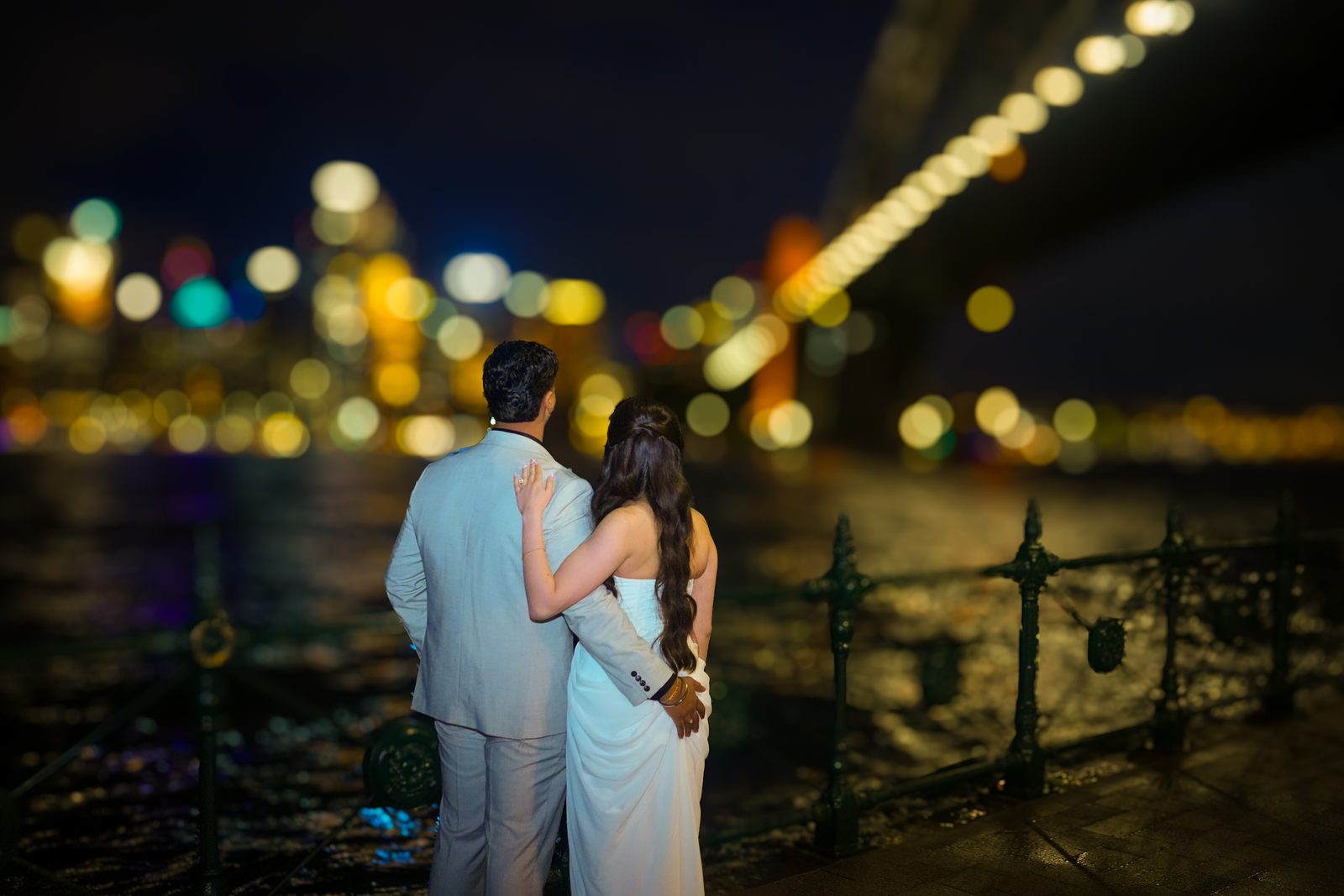 Newlyweds beneath the Sydney Harbour Bridge at night with the city skyline glowing behind them
