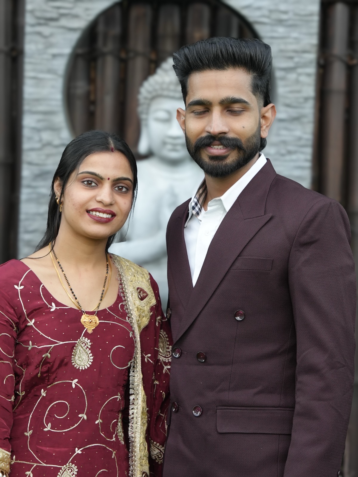 Prince and Sagandeep smiling together in front of a stone Buddha at their backyard elopement in Sydney