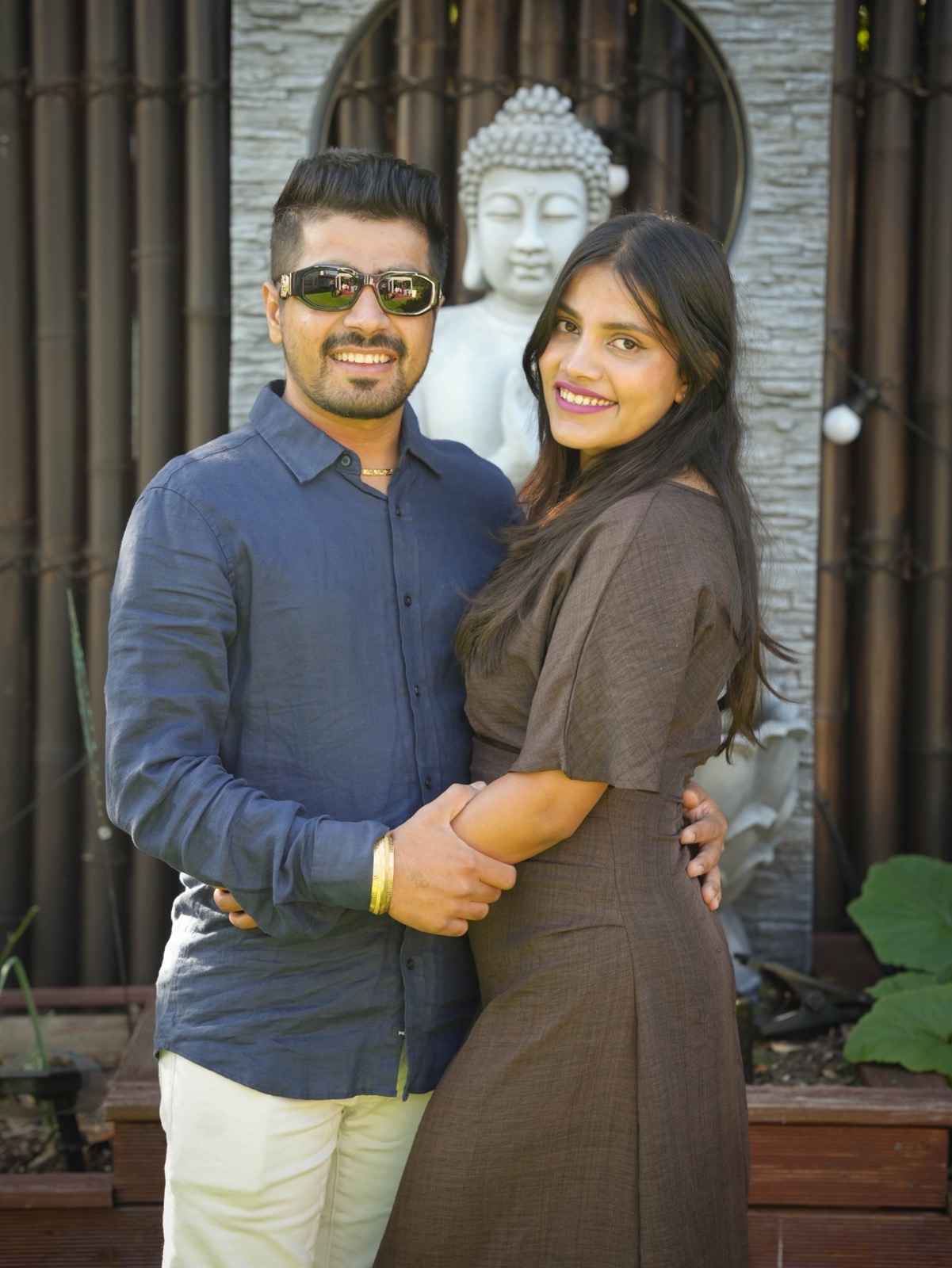 Sahil and Radhika smiling together in front of a stone Buddha at their registry-style wedding in Sydney