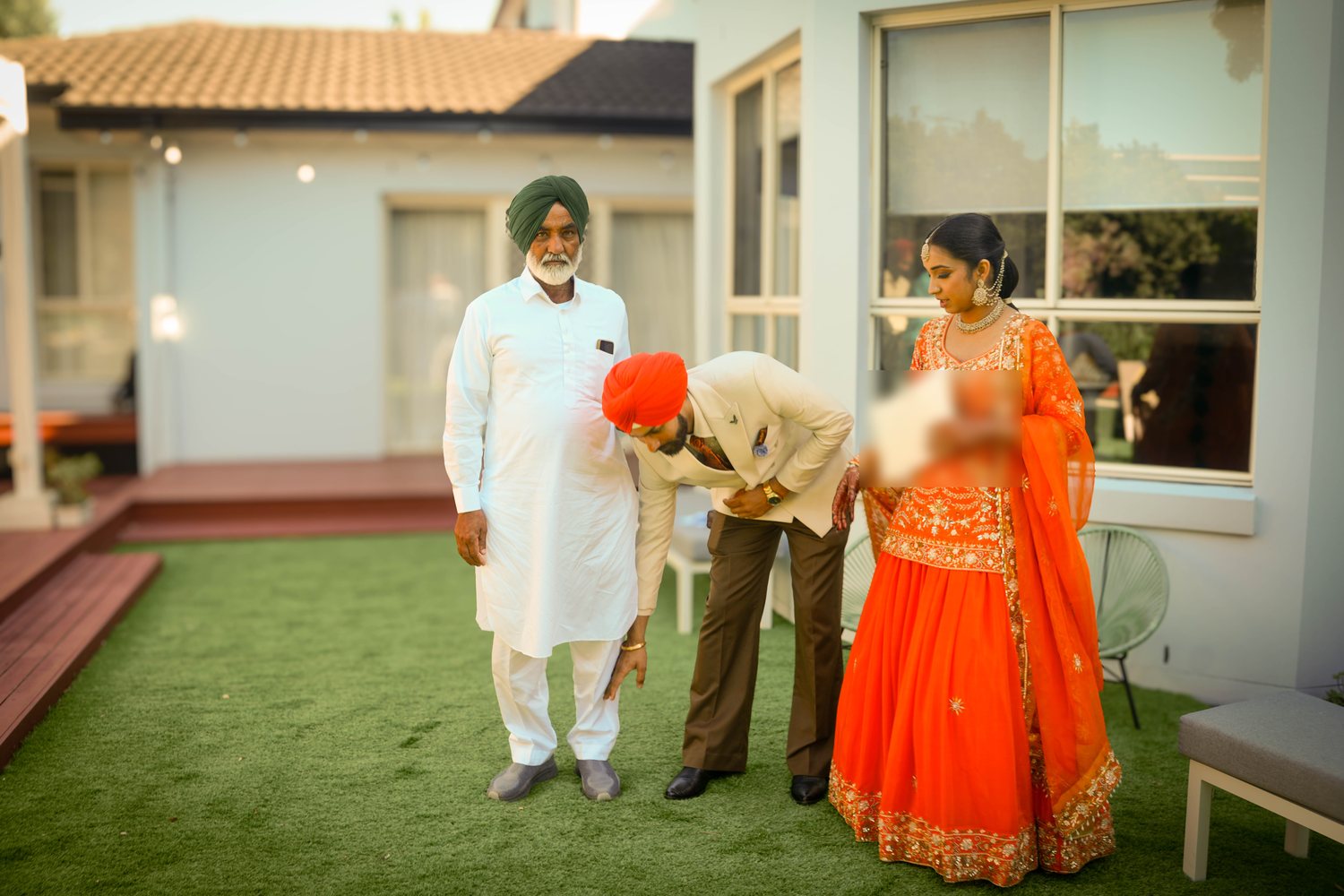A Sikh groom bowing to touch an elder's feet in respect after the ceremony, bride beside him holding the marriage certificate