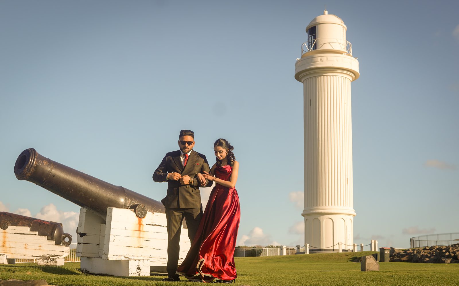 Lovepreet and Gurpinder standing arm in arm beside an old cannon with the white Wollongong lighthouse tower rising behind them