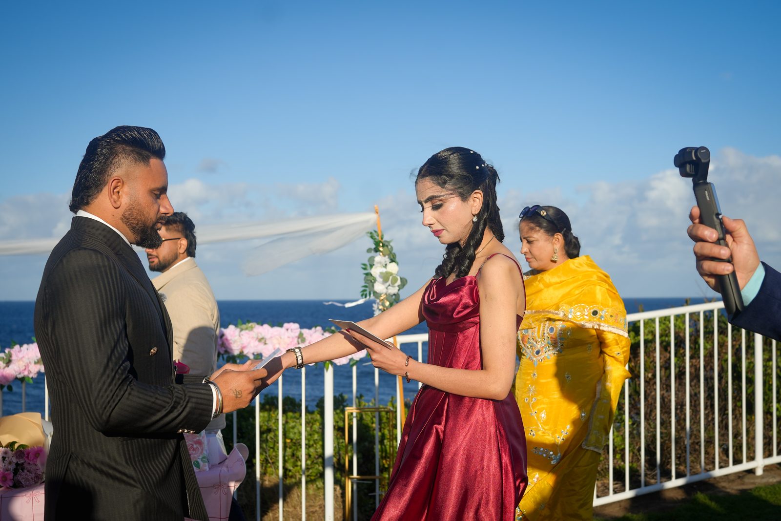 Lovepreet and Gurpinder reading their vows at their lighthouse wedding in Wollongong, with the ocean behind them and family looking on
